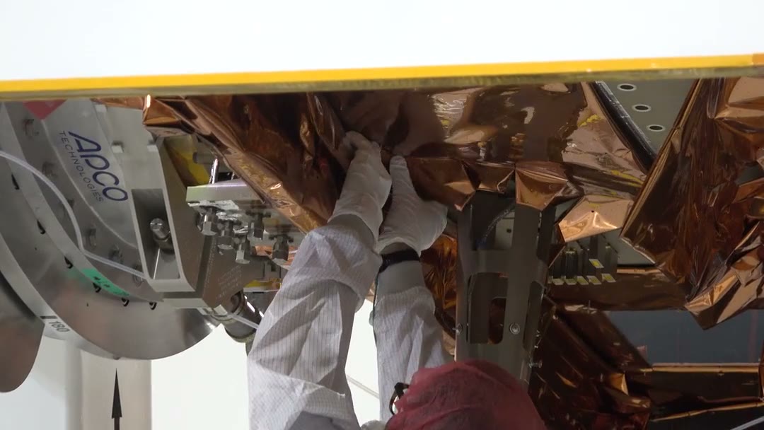 Technicians smoothing a gold insulation blanket onto the underside of the Sentinel-6B spacecraft.